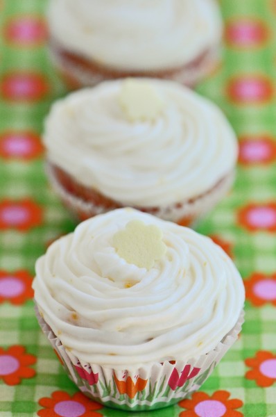 "Three mini lemon cupcakes, one behind the other sitting on an orange and pink flowered fabric"