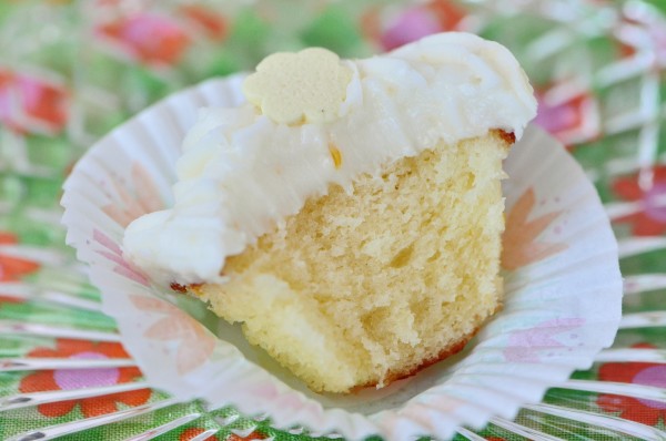 "Mini lemon cupcake with a bite taken out of it sitting on an opened white cupcake liner"