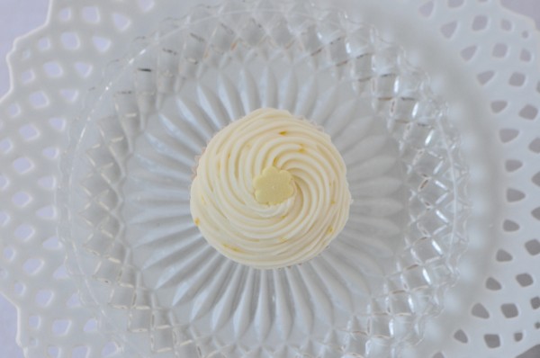"Mini lemon cupcake sitting on a cut glass plate, shot from above"